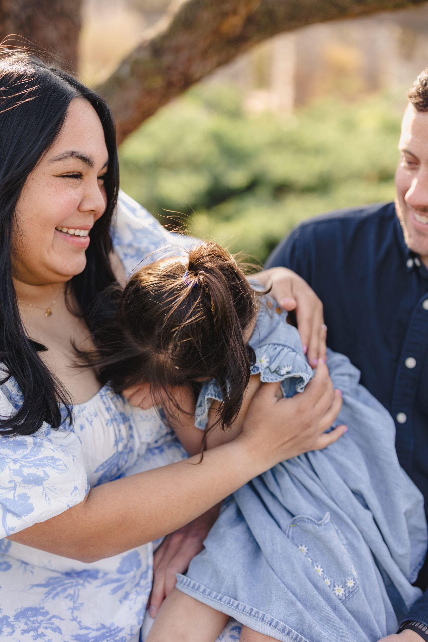 a family of three sitting together on a bench in loose park the little girl is hugging her mtoher