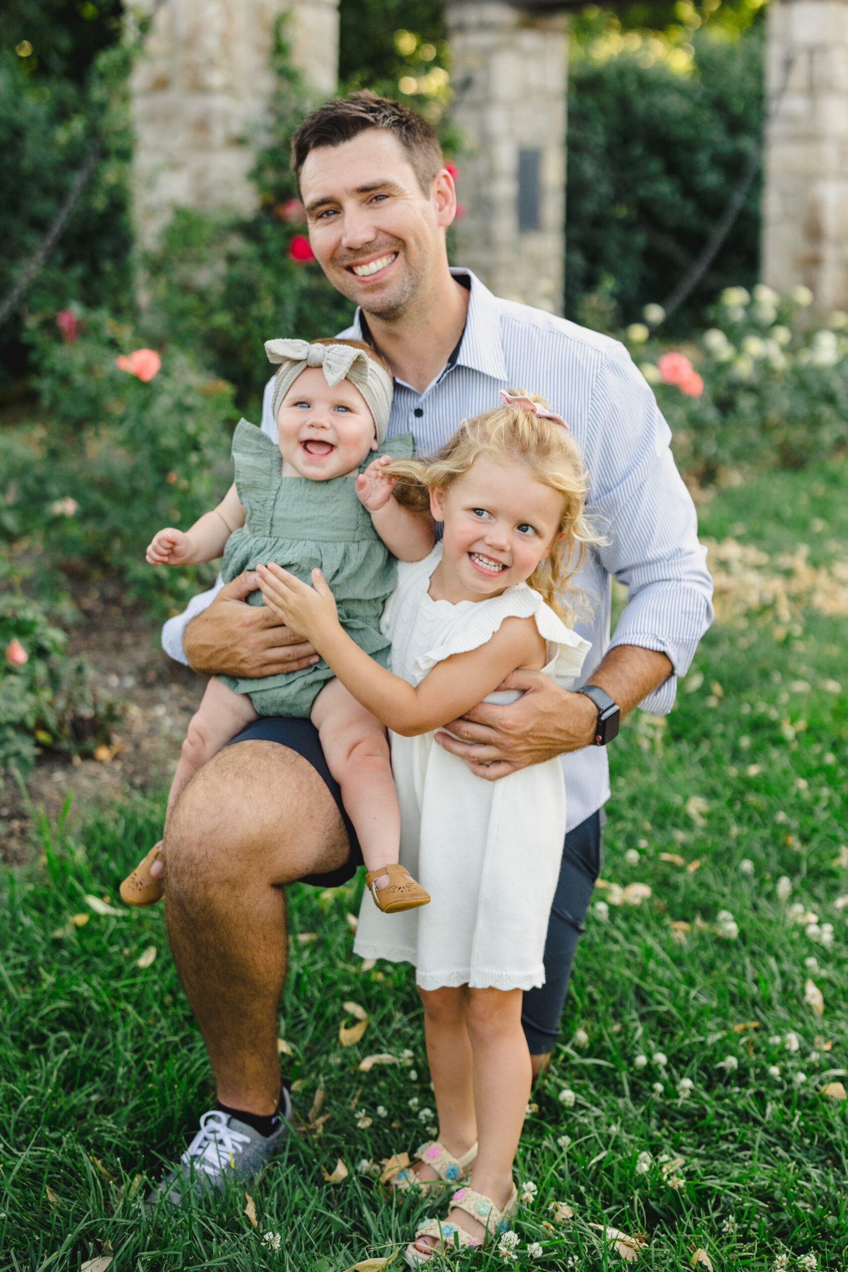 a father holding his two daughters in a park 