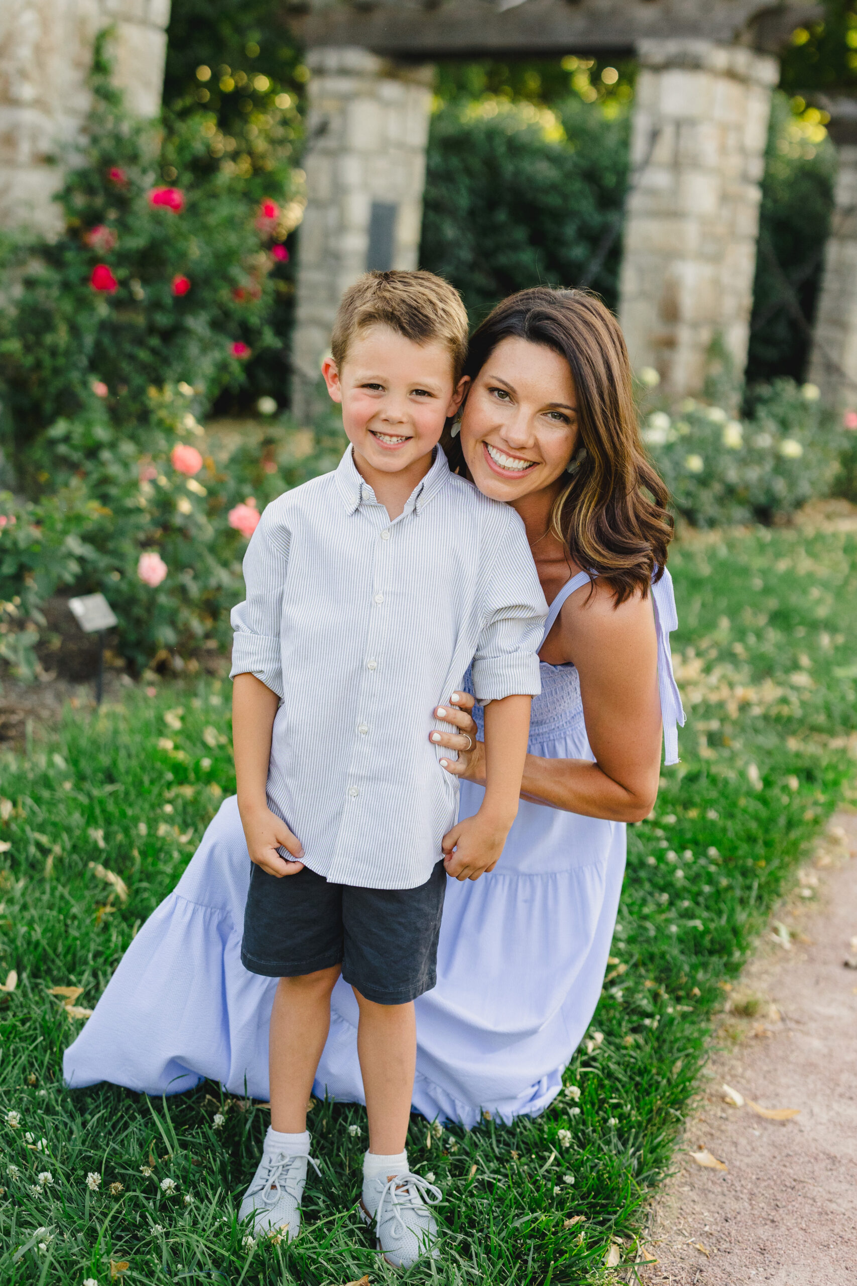 a mother taking a photo with her son in a park next to rose bushes 
