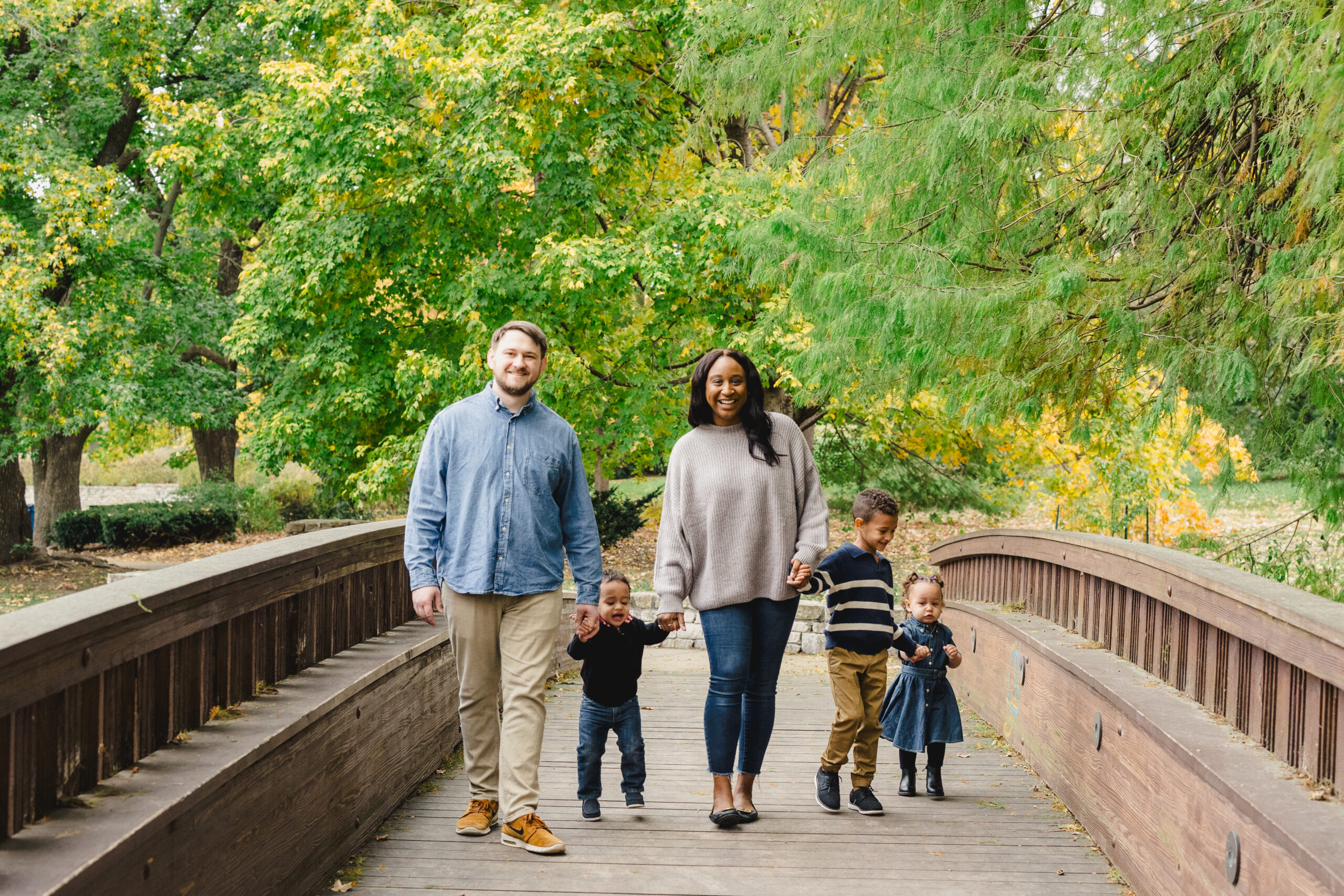 a family crossing the bridge in loose park together all holding hands 