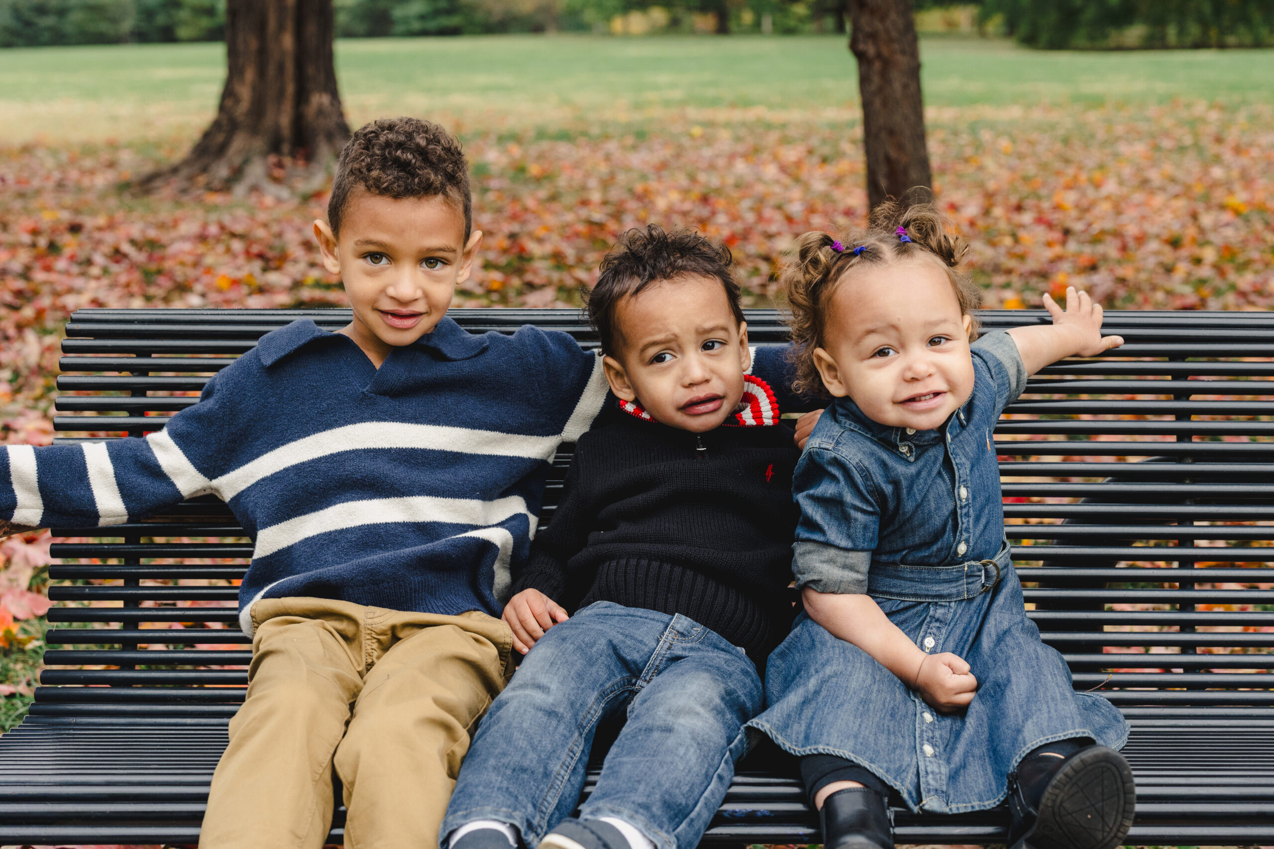 three siblings sitting next to each other on a bench in a park 