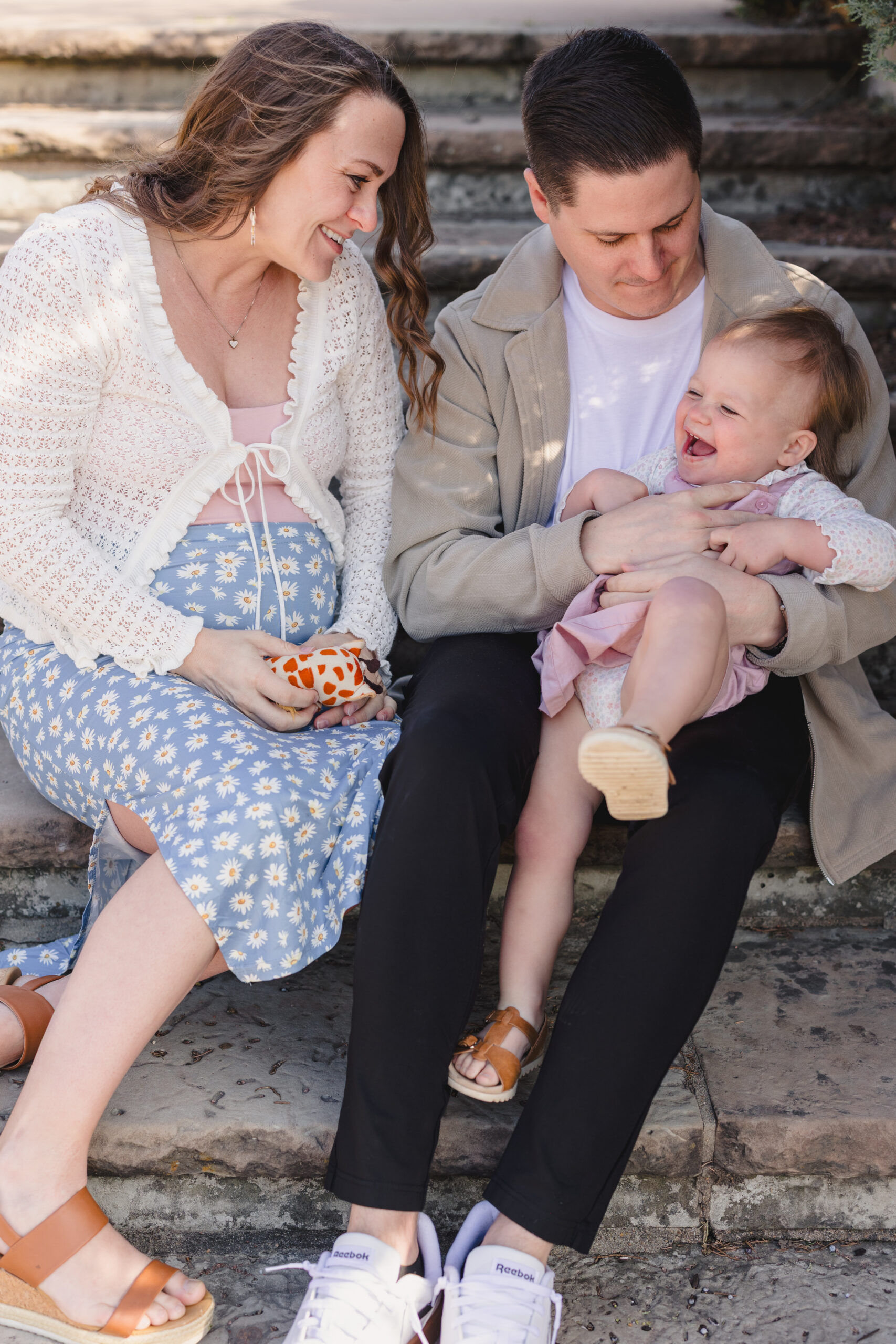 a mother and father playing with their daughter and sitting on steps 