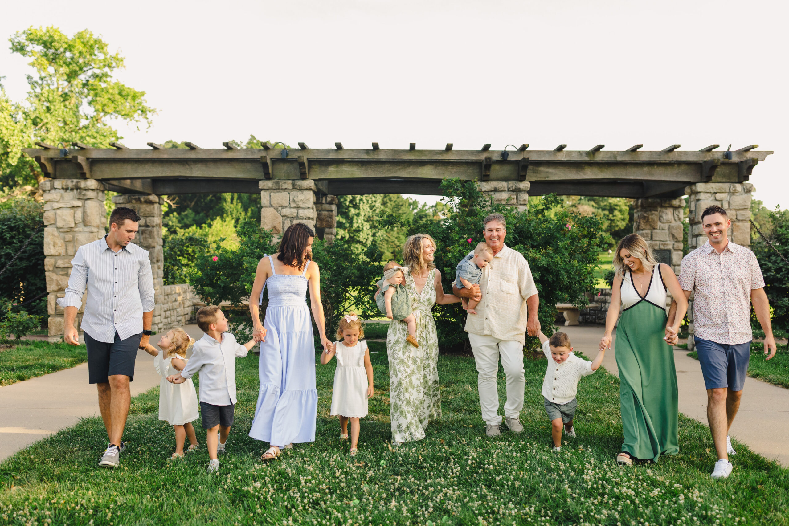 a family holding hands and walking across the grass together in loose park in summer in kansas city 