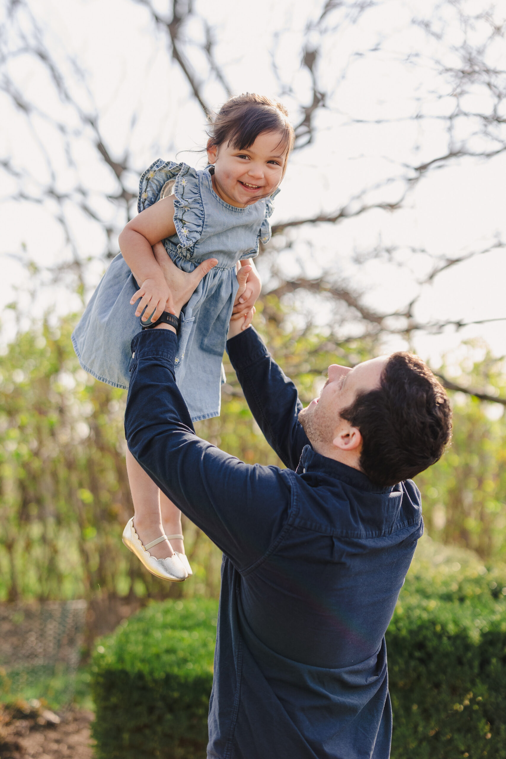 a father lifting his daughter up in the air in a park